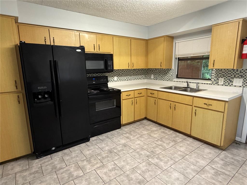 A kitchen features light wood cabinets, black appliances, a tiled backsplash, and light-colored floor tiles — 112 JASPER STREET, BUSHNELL, FL