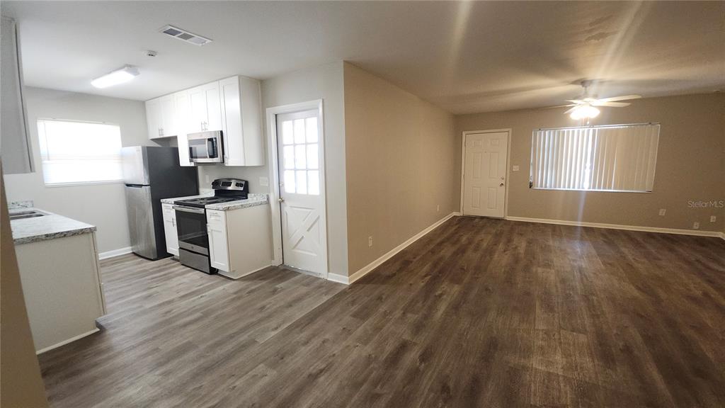 An open-concept kitchen and living area featuring white cabinets, stainless appliances, and wood-look flooring — 908 WESTMORE AVENUE, BRANDON, FL