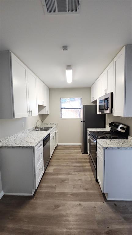 A galley kitchen features white cabinets, granite countertops, stainless steel appliances, and wood-look flooring — 908 WESTMORE AVENUE, BRANDON, FL