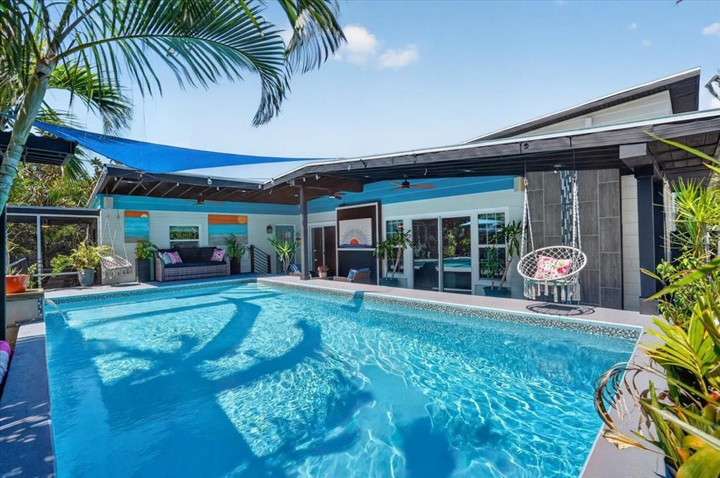 A swimming pool sits on a patio under a blue shade sail beside a house — 1520 60TH STREET S, GULFPORT, FL
