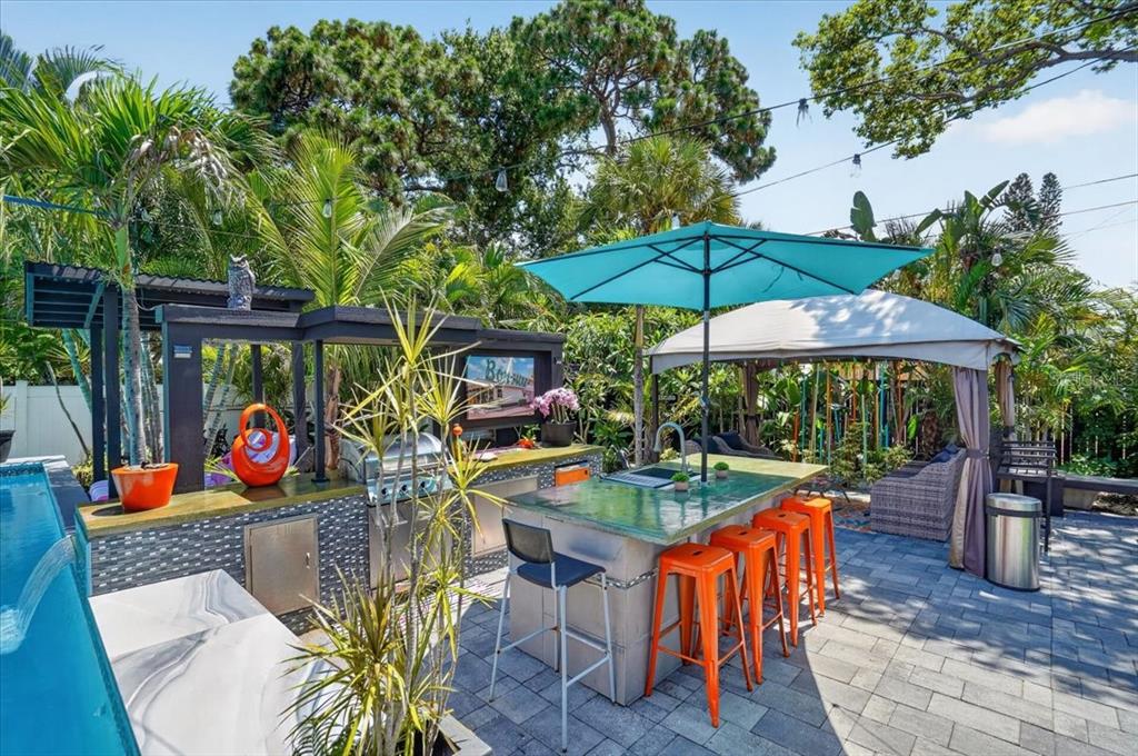 An outdoor kitchen with a bar, orange stools, and a turquoise umbrella beside a pool — 1520 60TH STREET S, GULFPORT, FL