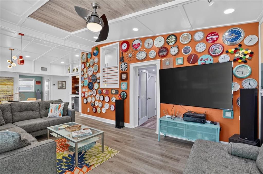 A living room features an orange wall covered in numerous clocks and a large television — 1520 60TH STREET S, GULFPORT, FL