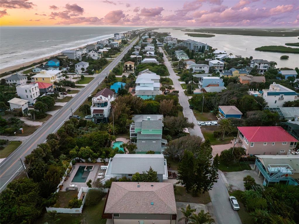 An aerial view shows a coastal neighborhood with houses, a road, and the ocean nearby — 6455 ENGRAM ROAD, NEW SMYRNA BEACH, FL