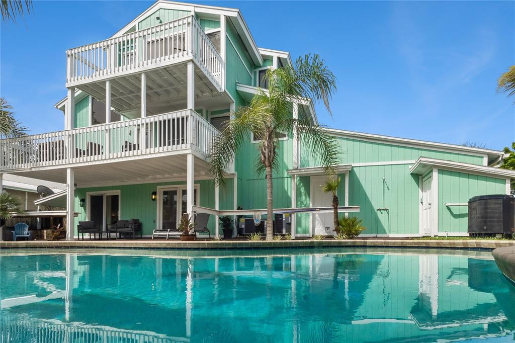 A three-story light green house with white balconies overlooks a backyard swimming pool — 6455 ENGRAM ROAD, NEW SMYRNA BEACH, FL