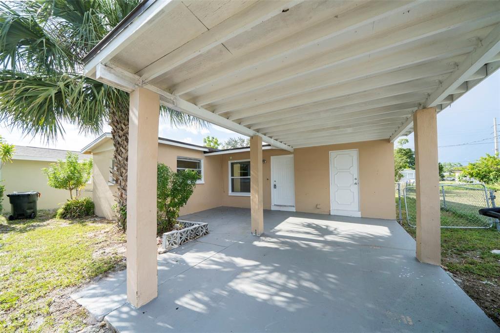 A covered concrete carport sits in front of a tan house with two white doors — 2985 SAINT CHARLES STREET, FORT MYERS, FL