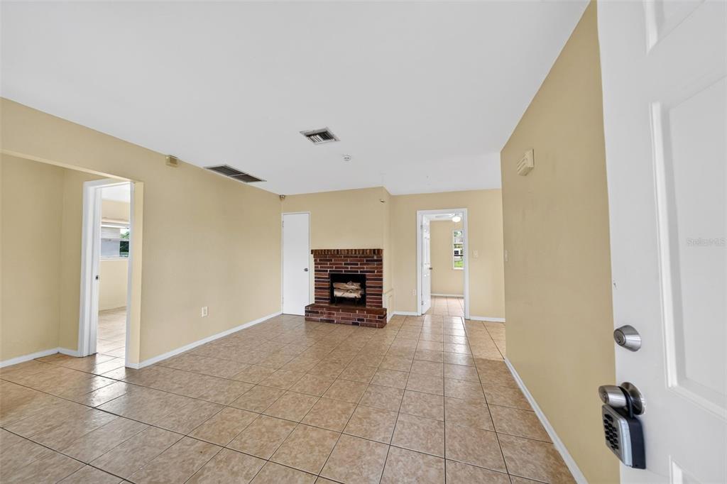 An interior view of a living room with tan walls, tile flooring, and a brick fireplace — 2985 SAINT CHARLES STREET, FORT MYERS, FL