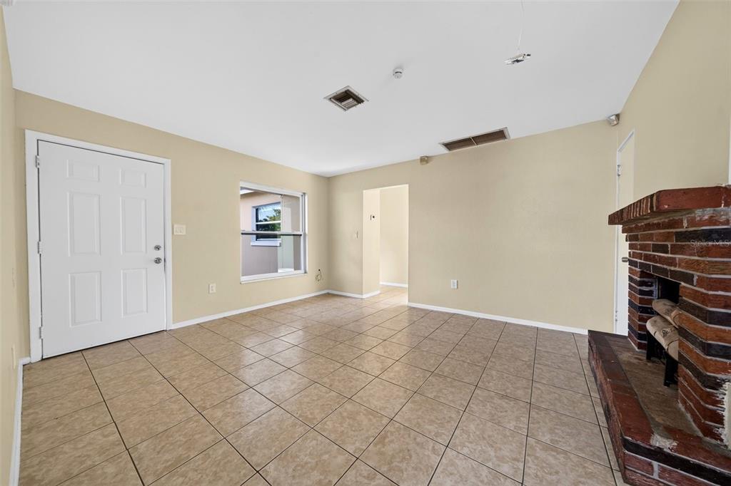 A living room with beige walls, tiled floors, a white door, and a brick fireplace — 2985 SAINT CHARLES STREET, FORT MYERS, FL