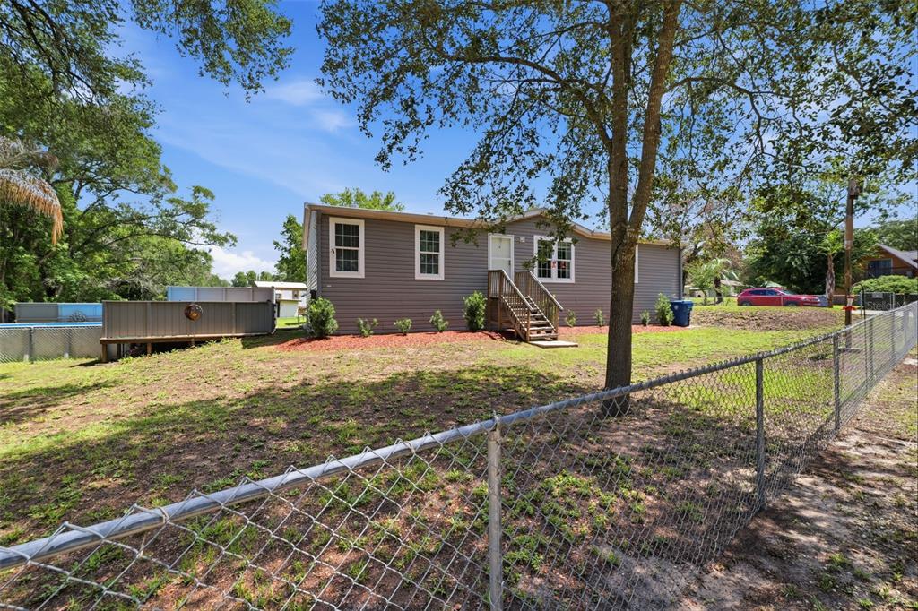 A gray single-story house with a wooden staircase stands behind a chain-link fence — 3183 CEDLEY ROAD, DADE CITY, FL