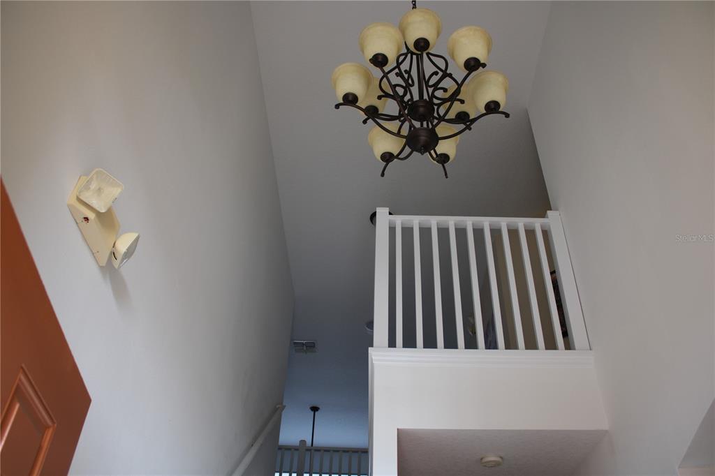 A high-ceilinged entryway features a large chandelier, white railings, and a wall-mounted light fixture — 463 PALOMA DRIVE, DAVENPORT, FL