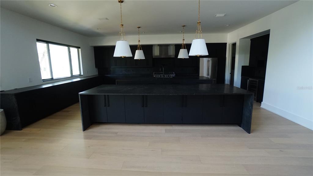 A modern kitchen features a large black island, matching cabinetry, and four white pendant lights — 4717 W ESTRELLA STREET, TAMPA, FL
