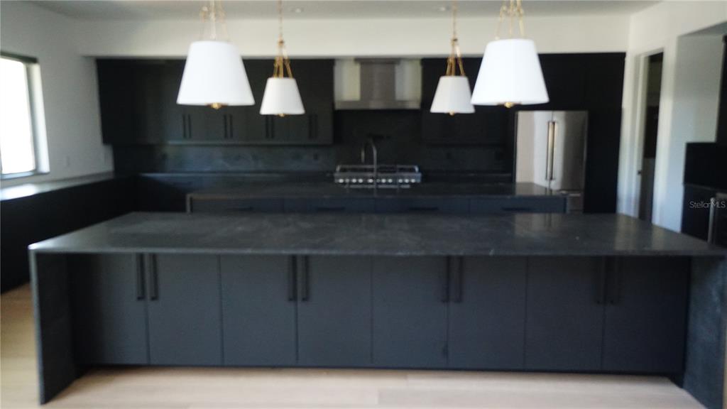 A modern kitchen features a large black island, dark cabinetry, and four white pendant lights — 4717 W ESTRELLA STREET, TAMPA, FL