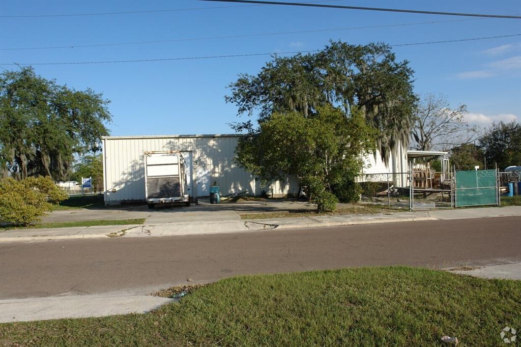 A single-story metal warehouse building sits behind a chain-link fence with a parked trailer — 1604 OLIVE STREET, LAKELAND, FL