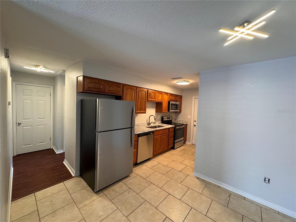 A kitchen features wood cabinets, stainless steel appliances, granite countertops, and light-colored tile flooring — 121 E PATTERSON STREET UNIT 123, LAKELAND, FL