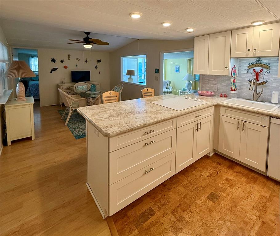 A kitchen with white cabinets and a stone-look island overlooks a dining and living area — 6091 PEONY ROAD, VENICE, FL