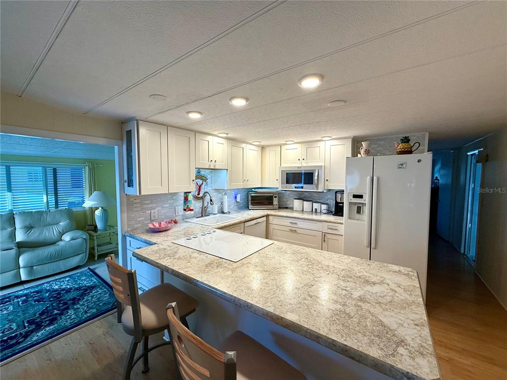 A kitchen with white cabinets, a stone-patterned countertop, and a breakfast bar with stools — 6091 PEONY ROAD, VENICE, FL