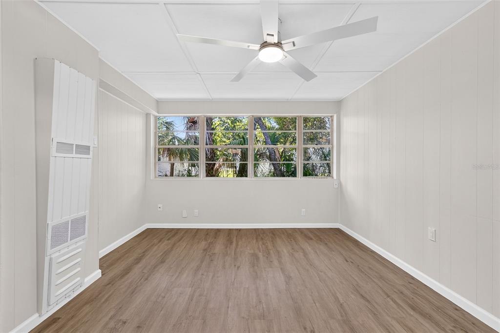 A room with light-colored paneled walls, wood-look flooring, a ceiling fan, and large windows — 1202 E CAROLINE STREET, TAVARES, FL