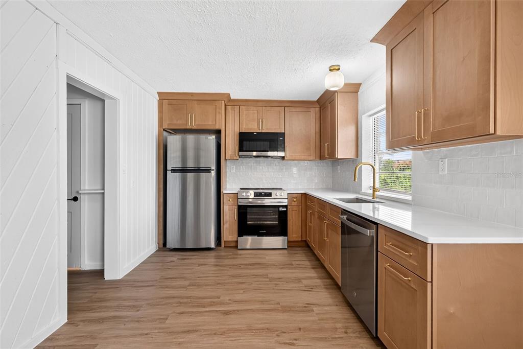 A kitchen features light wood cabinets, stainless steel appliances, white countertops, and wood-look flooring — 1202 E CAROLINE STREET, TAVARES, FL