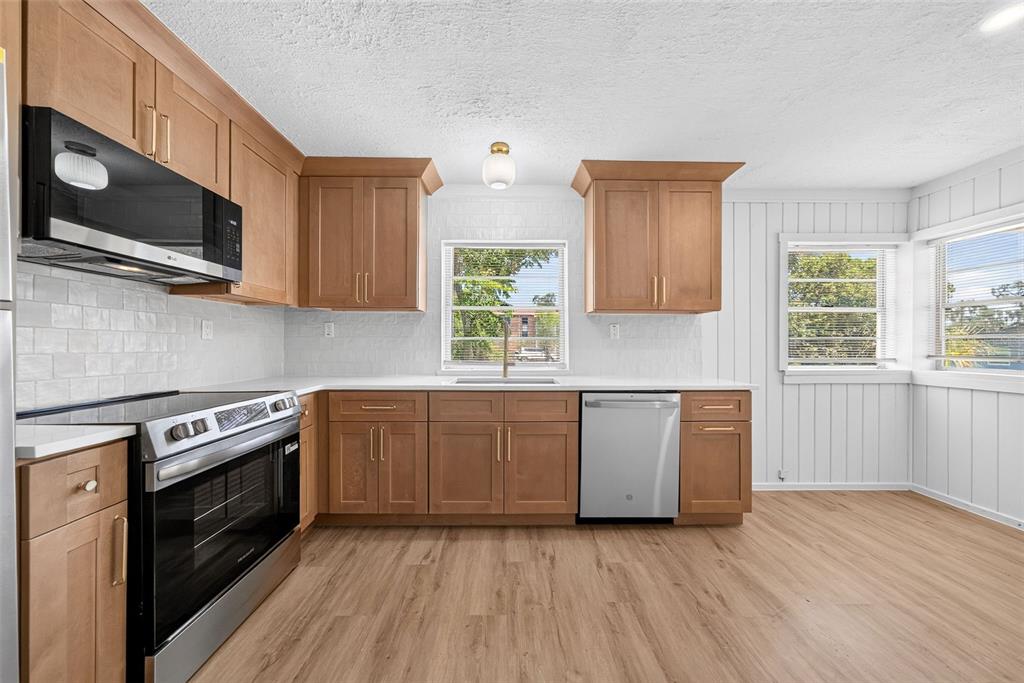 A kitchen features light wood cabinets, stainless steel appliances, white countertops, and light wood flooring — 1202 E CAROLINE STREET, TAVARES, FL