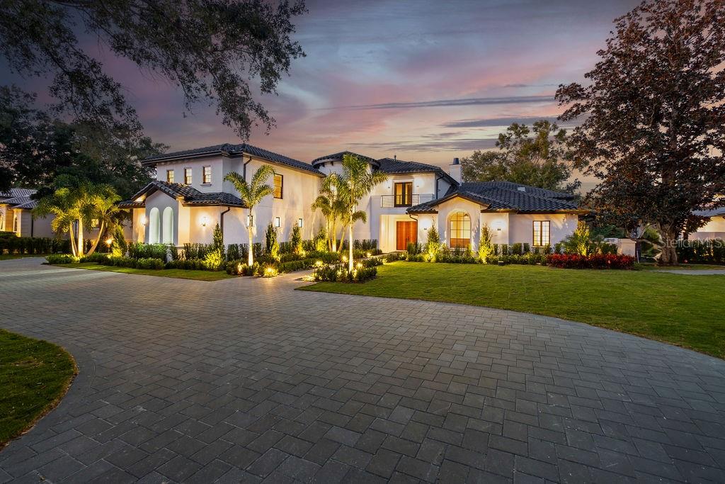 A two-story Mediterranean-style house with a paved circular driveway and illuminated landscaping at dusk — 9725 CHESTNUT RIDGE DRIVE, WINDERMERE, FL