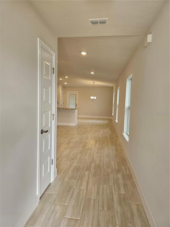 A hallway with light wood-look tile floors leads into an open-concept kitchen and dining area — 36109 TRINITY GLADE ROAD, DADE CITY, FL