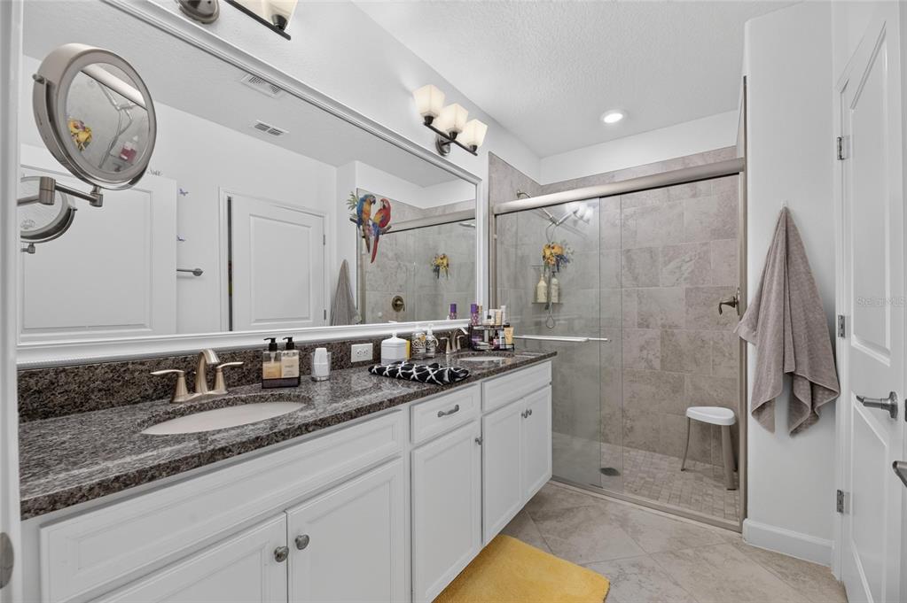 A bathroom features a double vanity with granite countertops, white cabinets, and a tiled shower — 5325 STOIC VALE DRIVE, WIMAUMA, FL