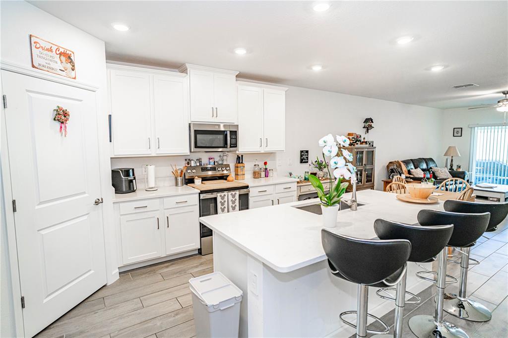 A kitchen with white cabinets, a large island with bar stools, and light wood-look flooring — 10857 RUSTIC EVE COURT, LAND O LAKES, FL