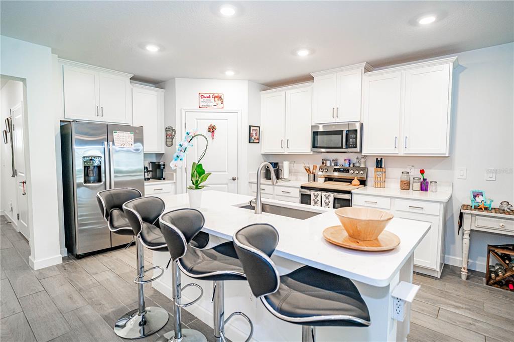A modern kitchen features white cabinetry, stainless steel appliances, a central island, and bar stools — 10857 RUSTIC EVE COURT, LAND O LAKES, FL