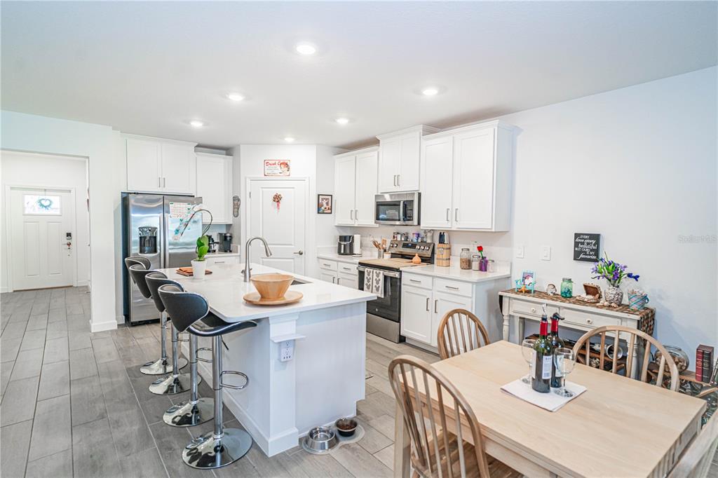 A kitchen features white cabinets, a central island with bar stools, and a dining table — 10857 RUSTIC EVE COURT, LAND O LAKES, FL