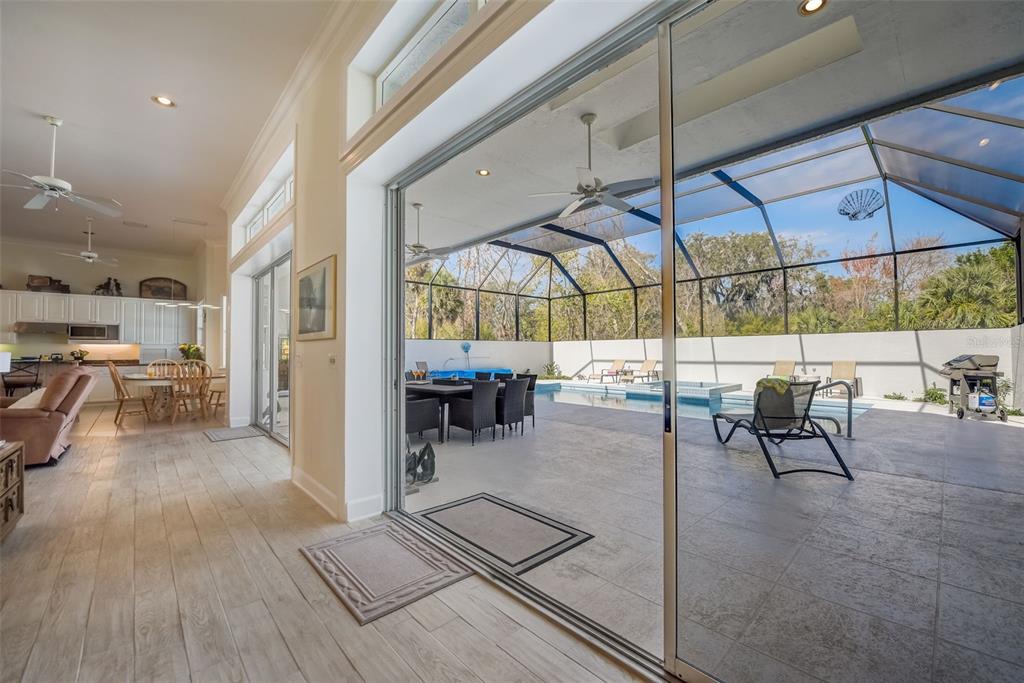 An open-concept living area with wood-look flooring leads to a screened-in patio and swimming pool — 4653 HADFIELD DRIVE, SARASOTA, FL
