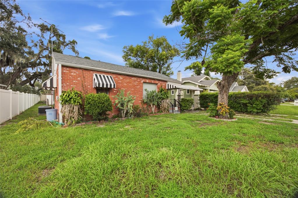 A side view of a single-story red brick house with a white fence and lawn — 1416 E IDLEWILD AVENUE, TAMPA, FL