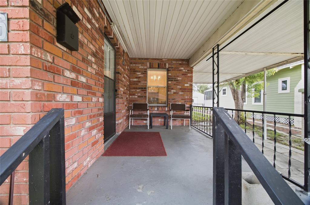 A covered brick porch features a concrete floor, two chairs, and a small side table — 1416 E IDLEWILD AVENUE, TAMPA, FL