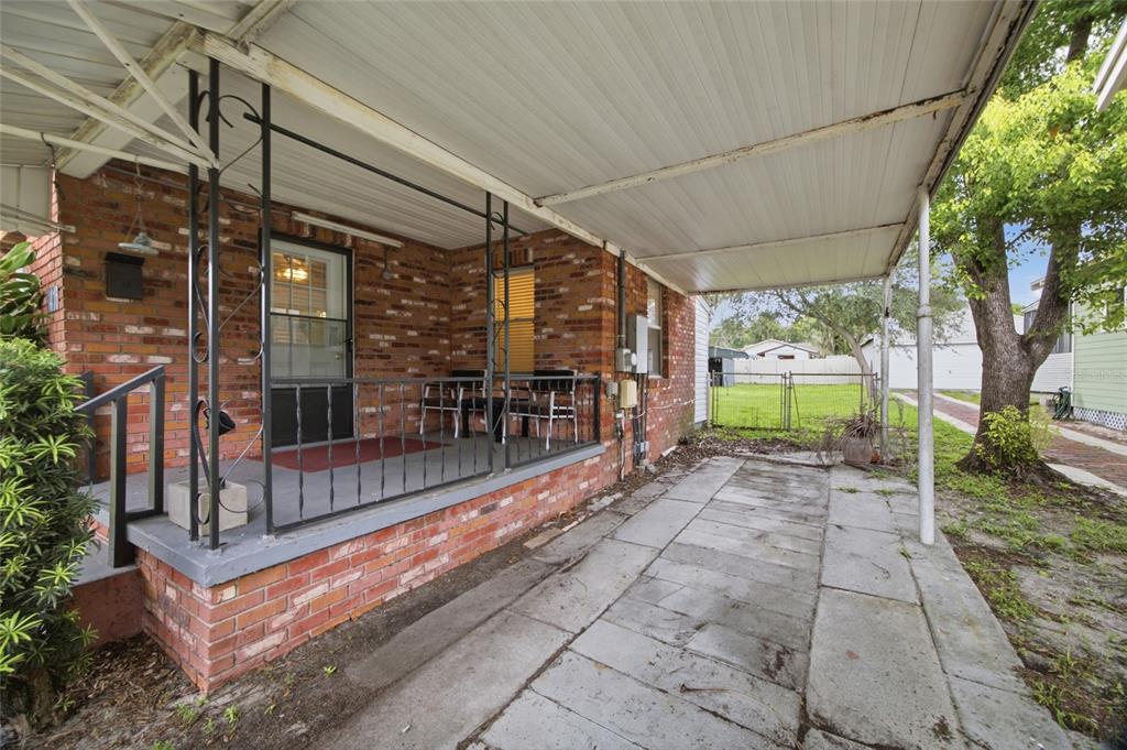 A brick house features a covered porch with metal railings and an adjacent concrete carport — 1416 E IDLEWILD AVENUE, TAMPA, FL