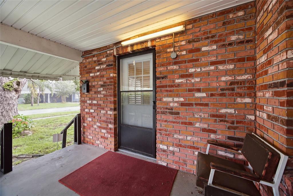 A covered brick porch features a storm door, a red rug, and a metal chair — 1416 E IDLEWILD AVENUE, TAMPA, FL