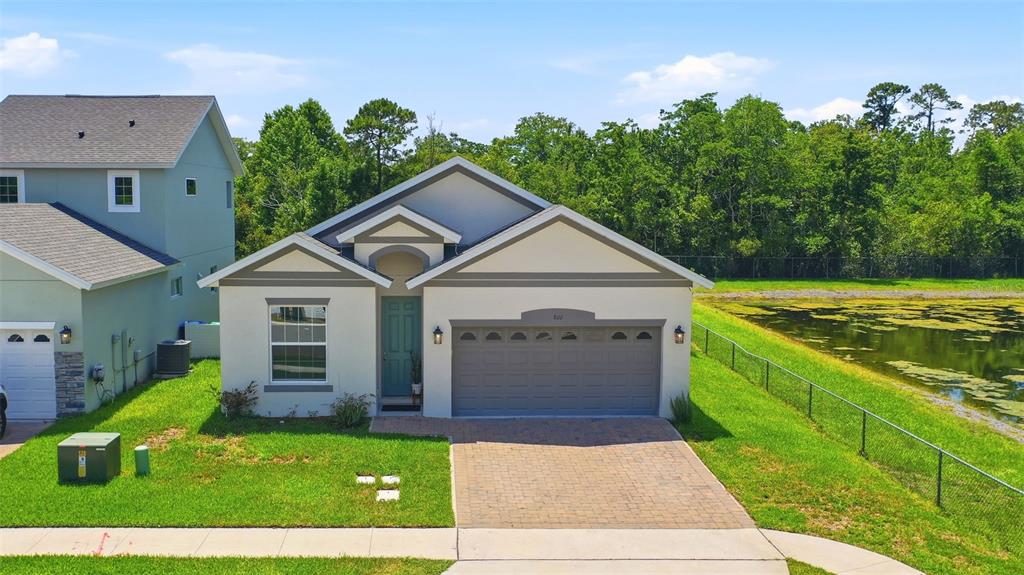 A single-story house with a teal front door, gray garage, and a pond in back — 802 REFLECTION LAKE DRIVE, ORLANDO, FL