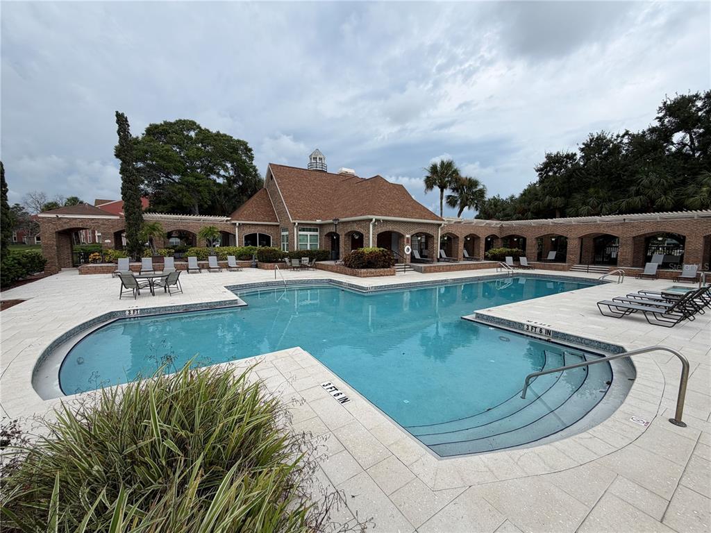An outdoor swimming pool with a surrounding patio and a brick clubhouse building — 10200 GANDY BOULEVARD N UNIT 418, ST PETERSBURG, FL