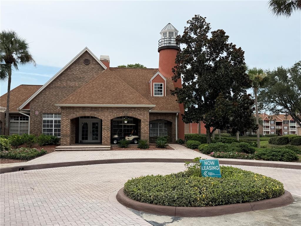 A brick building with a lighthouse-style tower stands behind a circular driveway and landscaping — 10200 GANDY BOULEVARD N UNIT 418, ST PETERSBURG, FL