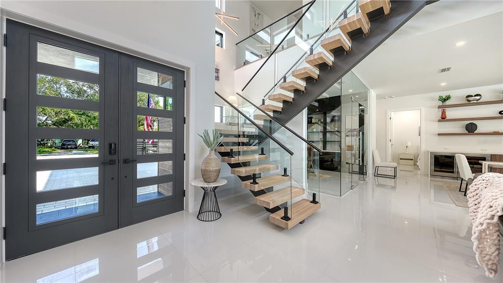 A modern entryway features a double front door, a floating staircase, and white tile flooring — 1960 BOYCE STREET, SARASOTA, FL