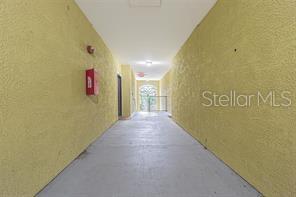 A narrow, outdoor apartment hallway with yellow textured walls and a concrete floor — 10205 COURTNEY PALMS BOULEVARD UNIT 304, TAMPA, FL