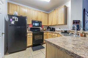 A kitchen features light wood cabinets, a black refrigerator, and a speckled laminate countertop — 10205 COURTNEY PALMS BOULEVARD UNIT 304, TAMPA, FL