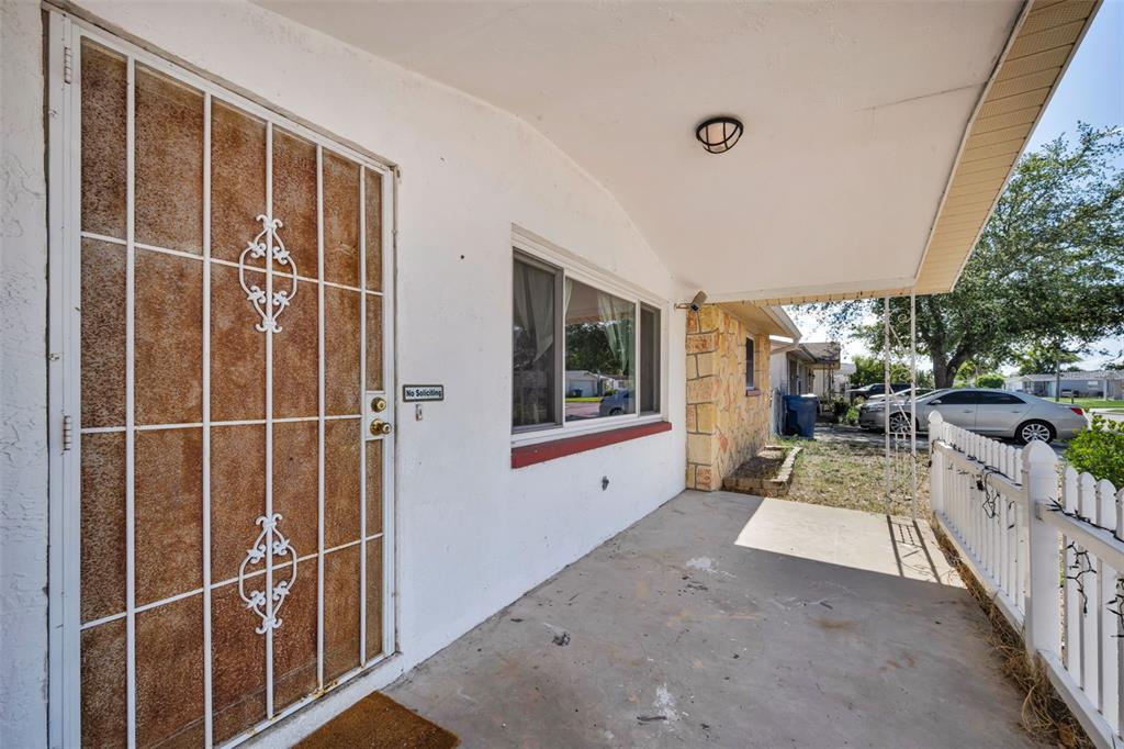 A covered concrete porch features a white security door and a white picket fence — 3541 BIGELOW DRIVE, HOLIDAY, FL