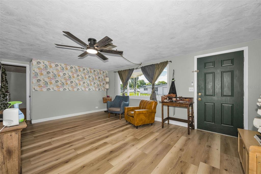 A living room features wood-look flooring, a floral accent wall, and a dark green front door — 3541 BIGELOW DRIVE, HOLIDAY, FL