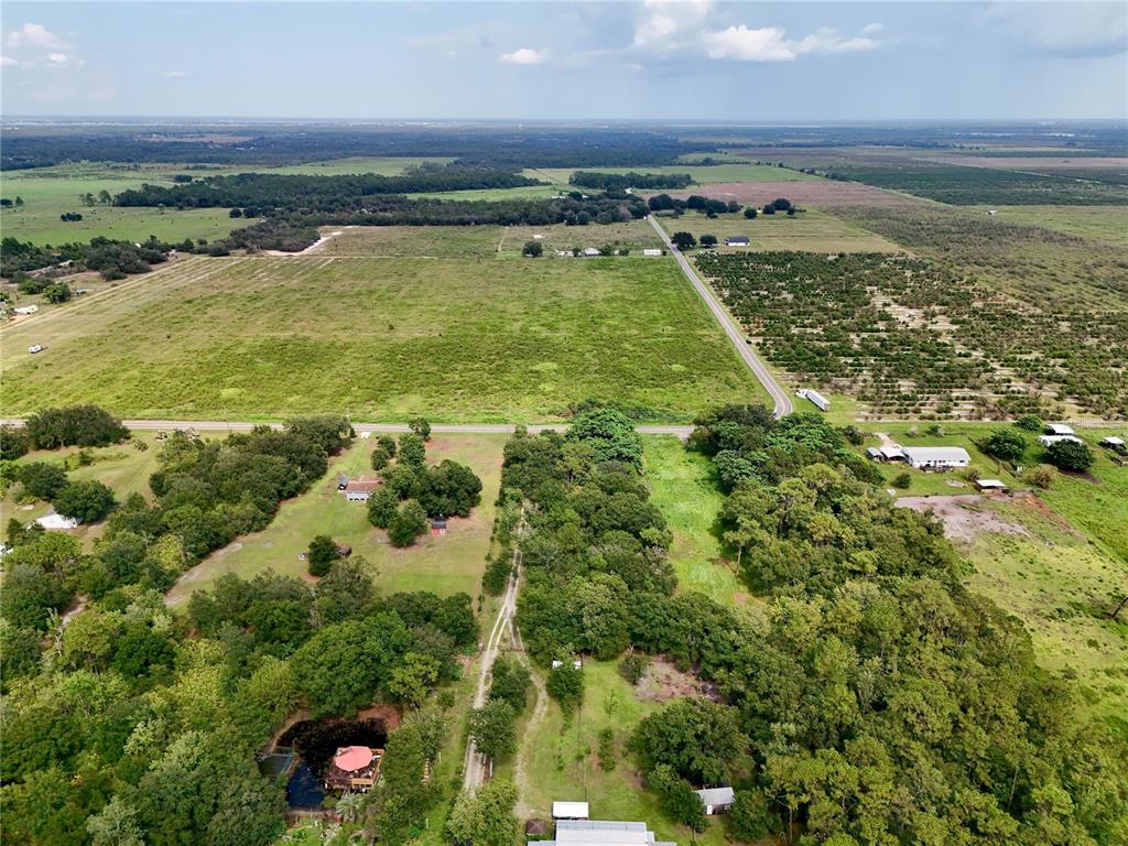 An aerial view shows a rural property with wooded areas, open fields, and a small pond — MCCLELLAN ROAD, FROSTPROOF, FL