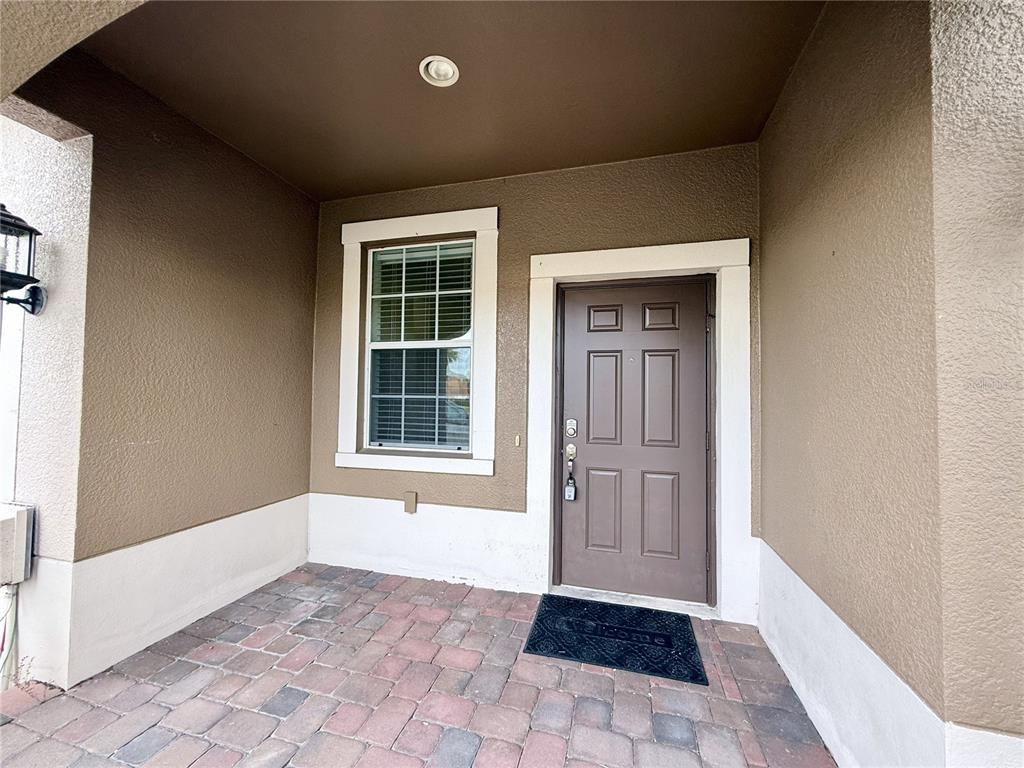 A brown front door and a window are set within a covered porch with pavers — 11155 SAVANNAH LANDING CIRCLE, ORLANDO, FL