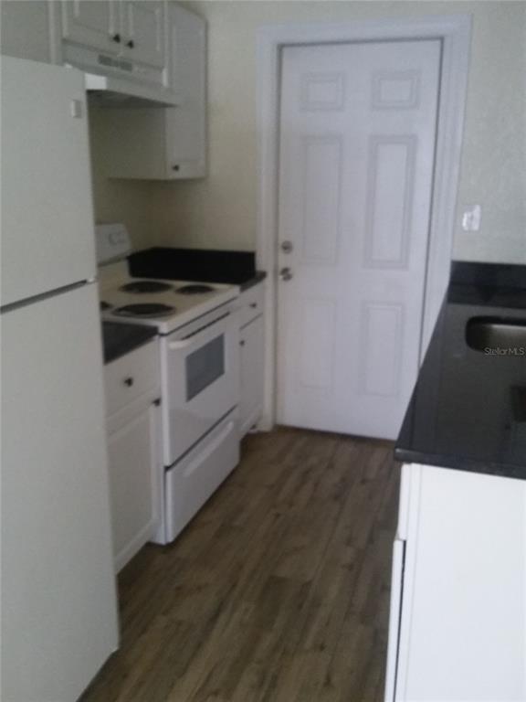 A kitchen features white cabinets, a white stove, a white refrigerator, and dark countertops — 1710 S WASHINGTON AVENUE UNIT 16, TITUSVILLE, FL