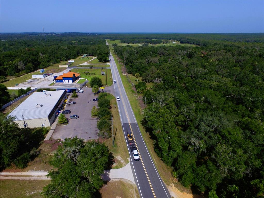 An aerial view shows a two-lane road passing by commercial buildings and dense forest — 24601 SE HIGHWAY 42, UMATILLA, FL
