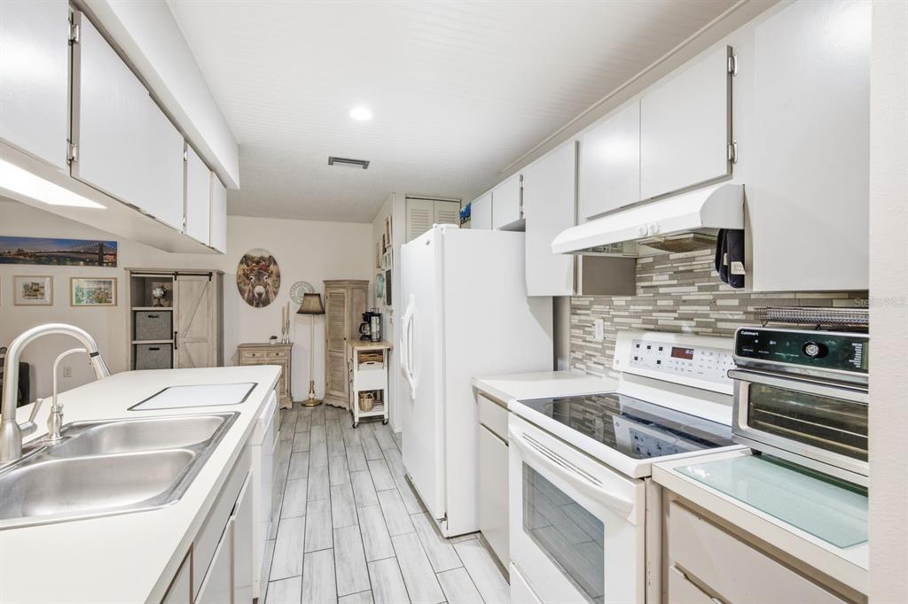A kitchen with white cabinets, stainless steel sink, white appliances, and light wood-look tile flooring — 10624 ENCINO COURT, PORT RICHEY, FL