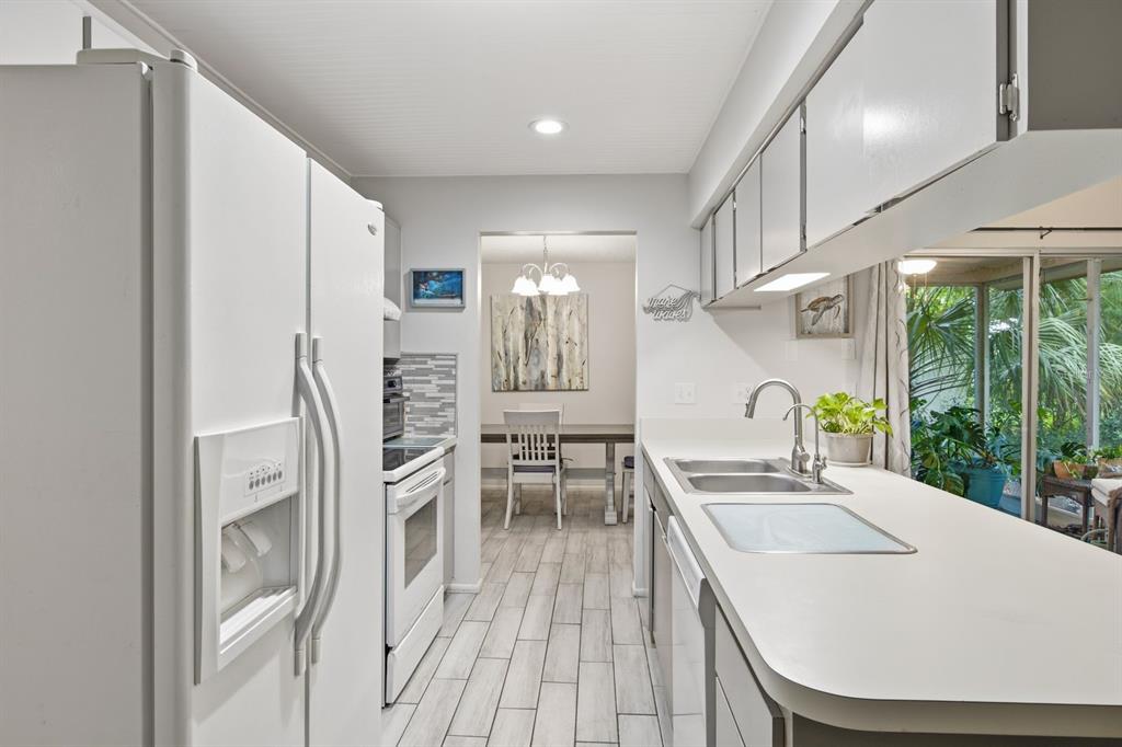 A white kitchen features light wood-look tile flooring, white cabinetry, and a view into the dining — 10624 ENCINO COURT, PORT RICHEY, FL