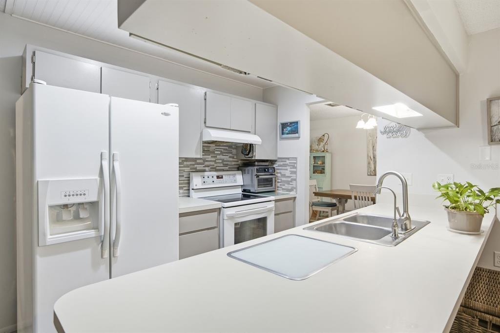 A kitchen with white appliances, light gray cabinets, a tiled backsplash, and a peninsula countertop — 10624 ENCINO COURT, PORT RICHEY, FL