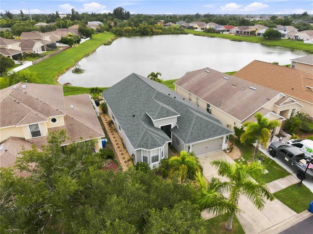 A grassy lawn slopes down to a pond surrounded by residential houses under a blue sky — 408 DURHAM SHORE COURT, APOLLO BEACH, FL
