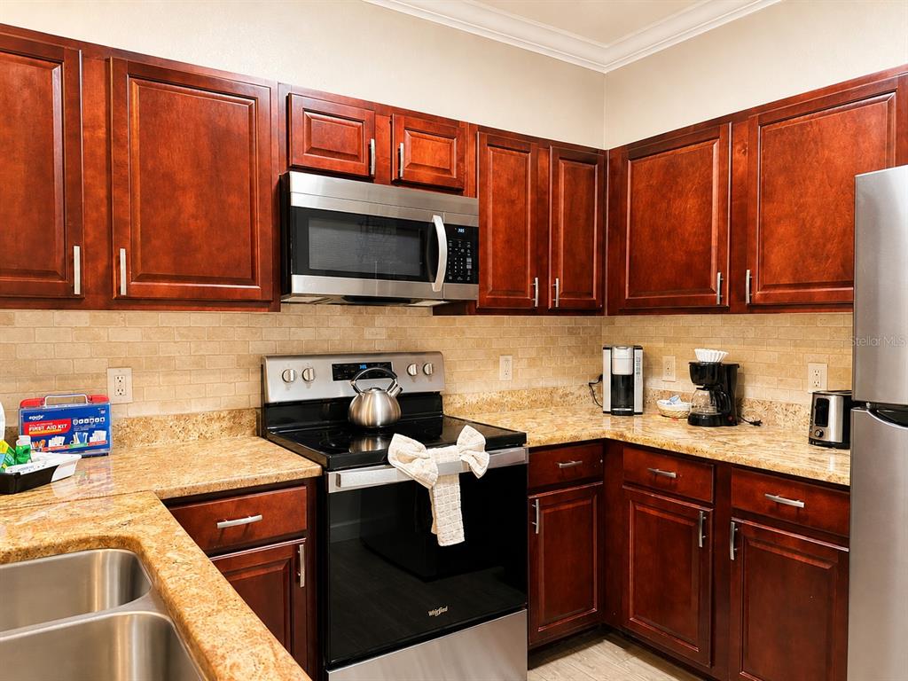 A kitchen features dark wood cabinets, granite countertops, stainless steel appliances, and a tiled backsplash — 1301 TUSCAN TERRACE UNIT 9205, DAVENPORT, FL